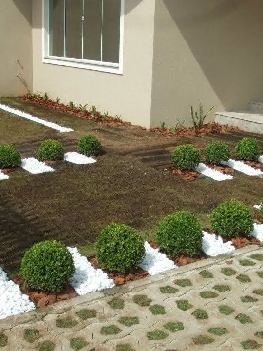 O mesmo quintal depois: caminho com dormentes integrado, buxinhos e pedras brancas decorativas