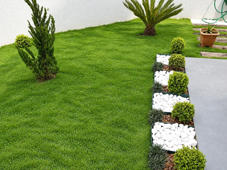 Projeto de paisagismo com gramado verde, canteiros geométricos com pedras brancas e buxinhos