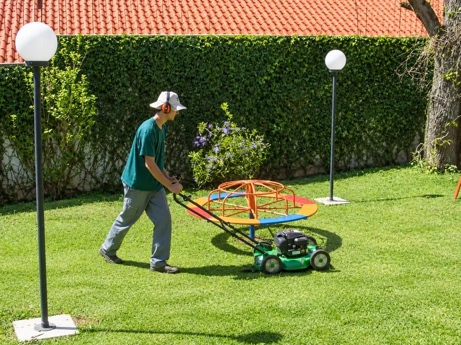 Jardineiro cortando a grama com cortador motorizado em quintal residencial